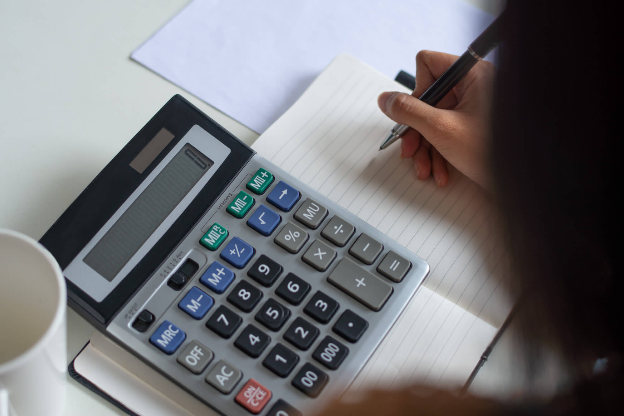 pessoa fazendo contas olhando para uma calculadora e um caderno