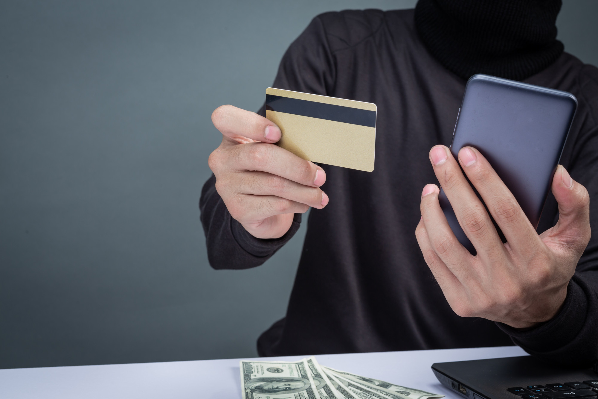 homem vestido de preto segurando um celular e um cartão na mão tentando dar um golpe