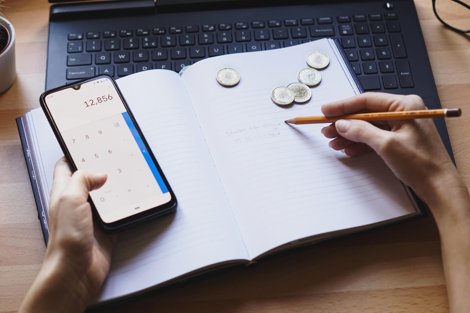 zoom de uma agenda com uma pessoa com o celular aberto na calculadora e algumas moedas do lado. a pessoa está fazendo contas e tentando se organizar financeiramente