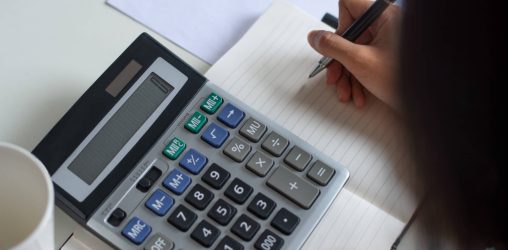 pessoa fazendo contas olhando para uma calculadora e um caderno