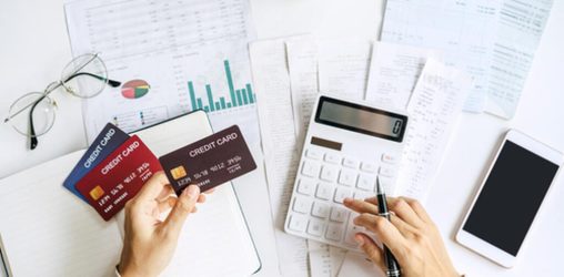 mesa com papeis, celular e cartões, juntamente com uma pessoa mexendo em uma calculadora, após lucrar com dicas de renda extra