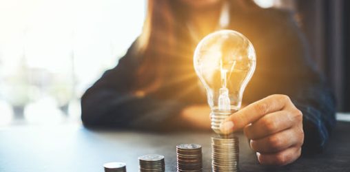 Mulher segurando lâmpada sobre pilha de moedas - Economizar energia