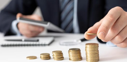 silhueta de um homem em frente a uma mesa fazendo contas e empilhando moedas tentando colocar as finanças em dia