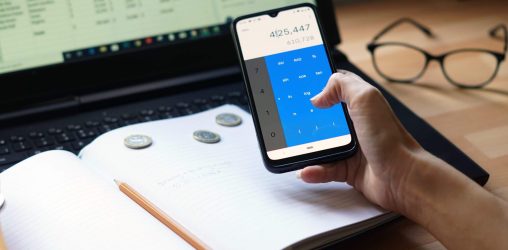pessoa segurando o celular e olhando para a tela do computador enquanto faz contas para organizar finanças