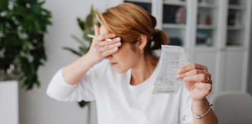 mulher cobrindo o rosto com a mão depois de ver boleto, pensando como fazer refinanciamento de dívidas