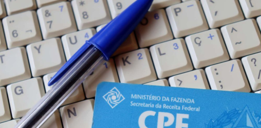 teclado de computador com uma caneta azul e um cartão de cpf em cima dele