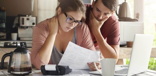 casal olhando para as suas contas na mesa da cozinha com semblante preocupado com vários papeis em cima da mesa e analisando a possibilidade de um empréstimo
